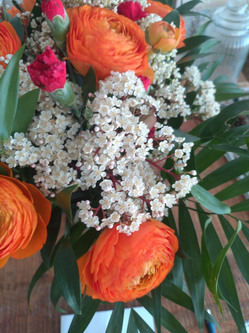 Auf dem Bild ist ein bunter Blumenstrauß mit auffälligen, orangefarbenen Ranunkeln zu sehen. Die Blüten stehen im Mittelpunkt der Nahaufnahme.